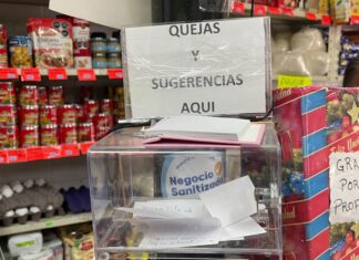 Escuchar también vende: la comunicación como ventaja invisible del pequeño comercio Caja de sugerencias y quejas colocada en el mostrador de una frutería, rodeada de productos, como muestra de comunicación directa entre comerciantes y clientes.
