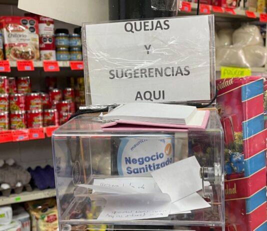 Escuchar también vende: la comunicación como ventaja invisible del pequeño comercio Caja de sugerencias y quejas colocada en el mostrador de una frutería, rodeada de productos, como muestra de comunicación directa entre comerciantes y clientes.