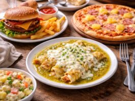 ¿Las enchiladas suizas son de Suiza? Mesa de madera con enchiladas suizas, hamburguesa con papas, pizza hawaiana y ensalada rusa, representando platillos con nombres de países que no siempre coinciden con su origen.