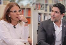 Entrevista censurada: Sabina Berman y Eduardo Verástegui debaten familia, libertad y aborto Dos personas sentadas frente a frente en un espacio tipo biblioteca, conversando durante una entrevista; una mujer viste de blanco y escucha con atención, mientras un hombre con traje gris habla y gesticula suavemente.