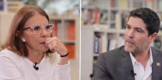 Entrevista censurada: Sabina Berman y Eduardo Verástegui debaten familia, libertad y aborto Dos personas sentadas frente a frente en un espacio tipo biblioteca, conversando durante una entrevista; una mujer viste de blanco y escucha con atención, mientras un hombre con traje gris habla y gesticula suavemente.