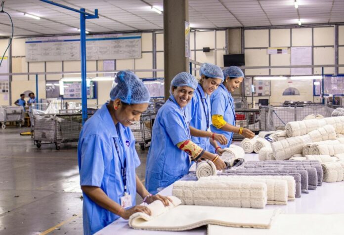 Trabajadoras con uniforme industrial azul revisan y doblan piezas textiles en una línea de producción dentro de una planta manufacturera.