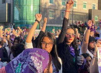 8M en México: por qué marchan las mujeres y qué caminos hay para cambiar la realidad Multitud de mujeres marchando durante el 8M con pañuelos morados y el puño en alto en señal de protesta y solidaridad.