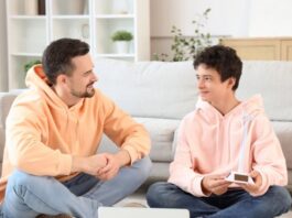 ¿Hablas con tus hijos? Padre e hijo adolescentes sentados en una sala de estar, conversando de manera cercana y relajada, generando un ambiente de confianza.