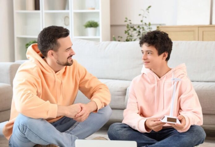 Padre e hijo adolescentes sentados en una sala de estar, conversando de manera cercana y relajada, generando un ambiente de confianza.