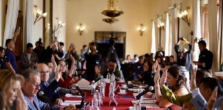 Tras el rechazo de la reforma electoral, el “Plan B” de Sheinbaum busca reducir costos políticos desde los estados y municipios Integrantes del Cabildo de San Luis Potosí levantan la mano durante una votación en una sesión oficial, con micrófonos y documentos sobre una mesa larga cubierta con mantel rojo.