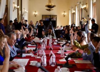 Tras el rechazo de la reforma electoral, el “Plan B” de Sheinbaum busca reducir costos políticos desde los estados y municipios Integrantes del Cabildo de San Luis Potosí levantan la mano durante una votación en una sesión oficial, con micrófonos y documentos sobre una mesa larga cubierta con mantel rojo.