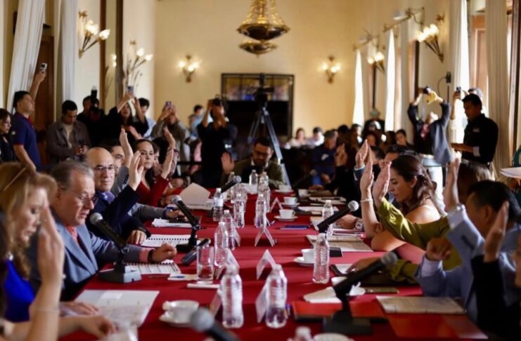 Tras el rechazo de la reforma electoral, el “Plan B” de Sheinbaum busca reducir costos políticos desde los estados y municipios Integrantes del Cabildo de San Luis Potosí levantan la mano durante una votación en una sesión oficial, con micrófonos y documentos sobre una mesa larga cubierta con mantel rojo.