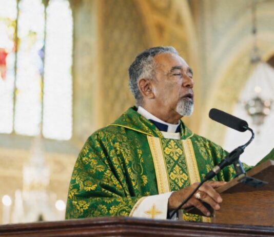 ¿Quién debe predicar en la Iglesia católica? Sacerdote católico predicando desde el ambón durante la homilía en una iglesia, vestido con casulla verde litúrgica.