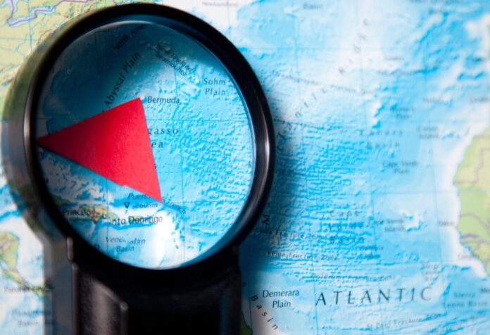 Mapa del océano Atlántico observado con una lupa que resalta el Triángulo de las Bermudas mediante una figura triangular roja.