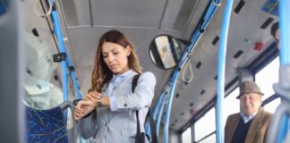 La vida cotidiana bajo presión: por qué sentimos que nunca tenemos tiempo (aunque sí lo tenemos) Mujer de pie dentro de un autobús urbano revisando su reloj, rodeada de otros pasajeros en un entorno cotidiano de transporte público.