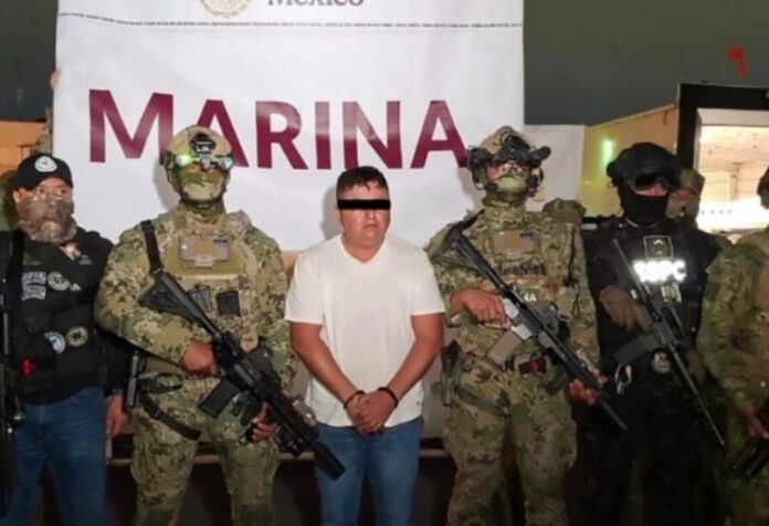 Hombre detenido con los ojos cubiertos, custodiado por elementos armados de la Marina y fuerzas de seguridad en México durante su presentación oficial.