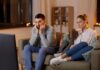 ¿Por qué cada vez vemos más sexo y drogas en películas y series? Familia sentada frente al televisor durante la noche mientras observa contenido audiovisual en un ambiente doméstico iluminado por la luz de la pantalla.