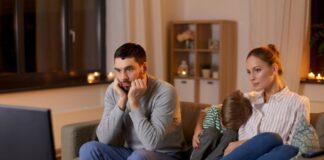 ¿Por qué cada vez vemos más sexo y drogas en películas y series? Familia sentada frente al televisor durante la noche mientras observa contenido audiovisual en un ambiente doméstico iluminado por la luz de la pantalla.