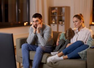¿Por qué cada vez vemos más sexo y drogas en películas y series? Familia sentada frente al televisor durante la noche mientras observa contenido audiovisual en un ambiente doméstico iluminado por la luz de la pantalla.