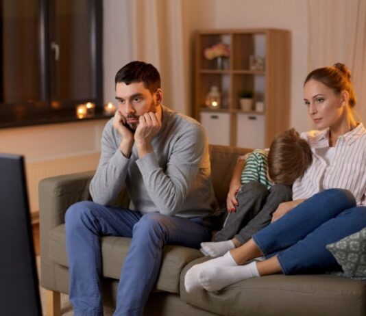 ¿Por qué cada vez vemos más sexo y drogas en películas y series? Familia sentada frente al televisor durante la noche mientras observa contenido audiovisual en un ambiente doméstico iluminado por la luz de la pantalla.