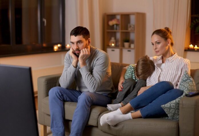 Familia viendo televisión Familia sentada frente al televisor durante la noche mientras observa contenido audiovisual en un ambiente doméstico iluminado por la luz de la pantalla.