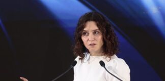 Ayuso regresa a España y describe un México que millones de mexicanos no reconocen Isabel Díaz Ayuso durante una conferencia en México, frente a dos micrófonos y con fondo oscuro iluminado en tonos azules.