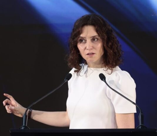 Ayuso regresa a España y describe un México que millones de mexicanos no reconocen Isabel Díaz Ayuso durante una conferencia en México, frente a dos micrófonos y con fondo oscuro iluminado en tonos azules.