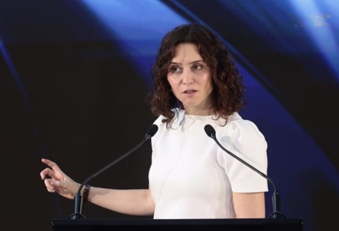 Isabel Díaz Ayuso durante una conferencia en México, frente a dos micrófonos y con fondo oscuro iluminado en tonos azules.