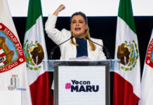 Maru Campos endurece su discurso contra Morena; el conflicto político entra en una nueva fase Maru Campos pronuncia un discurso desde un podio, con el puño levantado, frente a banderas de México y del estado de Chihuahua durante un acto político de apoyo.