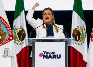 Maru Campos endurece su discurso contra Morena; el conflicto político entra en una nueva fase Maru Campos pronuncia un discurso desde un podio, con el puño levantado, frente a banderas de México y del estado de Chihuahua durante un acto político de apoyo.