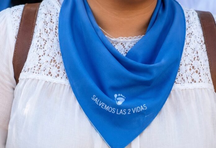 Primer plano de una mujer portando un pañuelo azul con la frase “Salvemos las 2 vidas”, símbolo utilizado en movilizaciones provida en México.