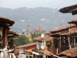México también se descubre caminando despacio Calles de un Pueblo Mágico mexicano con techos de teja y una iglesia al fondo entre montañas y neblina.