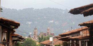 México también se descubre caminando despacio Calles de un Pueblo Mágico mexicano con techos de teja y una iglesia al fondo entre montañas y neblina.
