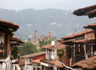 México también se descubre caminando despacio Calles de un Pueblo Mágico mexicano con techos de teja y una iglesia al fondo entre montañas y neblina.