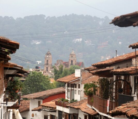 México también se descubre caminando despacio Calles de un Pueblo Mágico mexicano con techos de teja y una iglesia al fondo entre montañas y neblina.