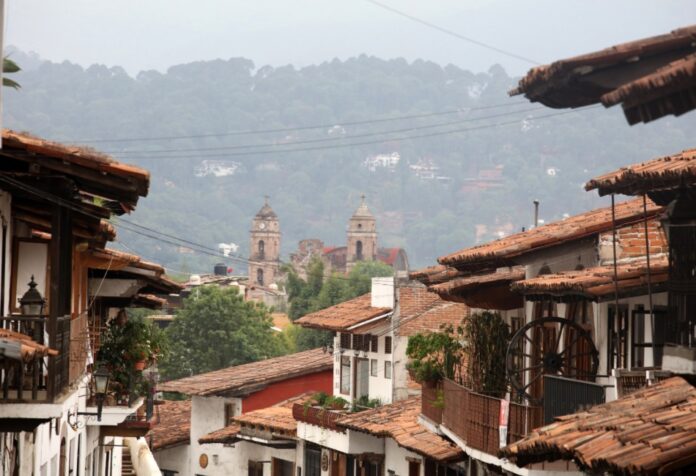 Calles de un Pueblo Mágico mexicano con techos de teja y una iglesia al fondo entre montañas y neblina.