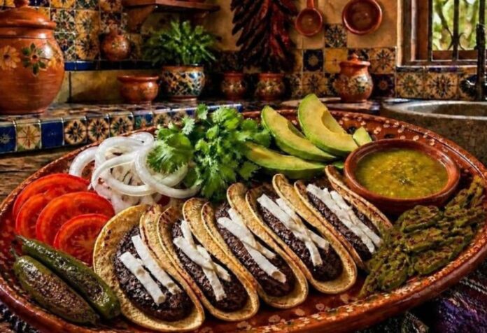 Tacos de frijol Plato de barro con tacos de frijol acompañados de aguacate, nopales asados, salsa verde, jitomate y cebolla en una cocina de estilo mexicano tradicional.