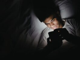 Dormir con el celular fuera de la habitación: un pequeño cambio que puede mejorar tu descanso Persona acostada en una cama utilizando un teléfono celular en una habitación oscura durante la noche, iluminada únicamente por la luz de la pantalla.
