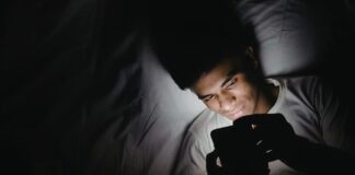 Dormir con el celular fuera de la habitación: un pequeño cambio que puede mejorar tu descanso Persona acostada en una cama utilizando un teléfono celular en una habitación oscura durante la noche, iluminada únicamente por la luz de la pantalla.