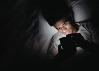 Dormir con el celular fuera de la habitación: un pequeño cambio que puede mejorar tu descanso Persona acostada en una cama utilizando un teléfono celular en una habitación oscura durante la noche, iluminada únicamente por la luz de la pantalla.