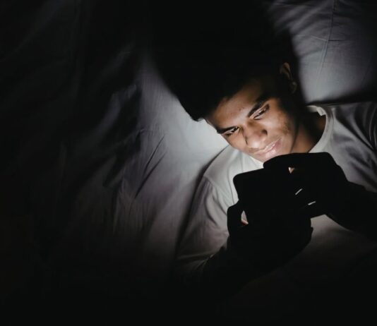 Dormir con el celular fuera de la habitación: un pequeño cambio que puede mejorar tu descanso Persona acostada en una cama utilizando un teléfono celular en una habitación oscura durante la noche, iluminada únicamente por la luz de la pantalla.
