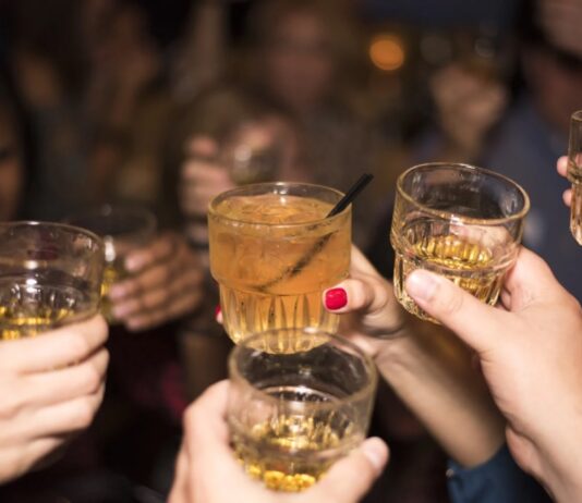 Jóvenes, alcohol y nuevas formas de divertirse Grupo de jóvenes brindando con bebidas alcohólicas durante una reunión nocturna, imagen que ilustra un artículo sobre el ocio juvenil y el consumo de alcohol en España y México.