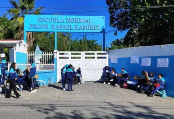 Hay menos profesores Entrada de la Escuela Normal Urbana Federal “Prof. Rafael Ramírez”, en Guerrero, con estudiantes reunidos en el exterior de las instalaciones.