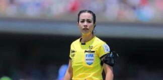 Katia Itzel García se prepara para otro capítulo histórico en el arbitraje mexicano Katia Itzel García, árbitra mexicana con uniforme amarillo de la FIFA, observa una jugada durante un partido en un estadio lleno de aficionados.