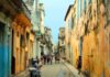 Cuba busca nuevas rutas para enfrentar su crisis económica Vista de una calle tradicional de La Habana, Cuba, con edificios antiguos de fachadas desgastadas y personas caminando en un entorno urbano característico de la isla.