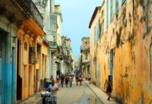 Cuba busca nuevas rutas para enfrentar su crisis económica Vista de una calle tradicional de La Habana, Cuba, con edificios antiguos de fachadas desgastadas y personas caminando en un entorno urbano característico de la isla.
