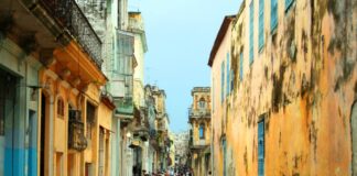 Cuba busca nuevas rutas para enfrentar su crisis económica Vista de una calle tradicional de La Habana, Cuba, con edificios antiguos de fachadas desgastadas y personas caminando en un entorno urbano característico de la isla.