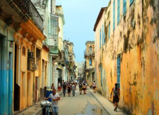 Cuba busca nuevas rutas para enfrentar su crisis económica Vista de una calle tradicional de La Habana, Cuba, con edificios antiguos de fachadas desgastadas y personas caminando en un entorno urbano característico de la isla.