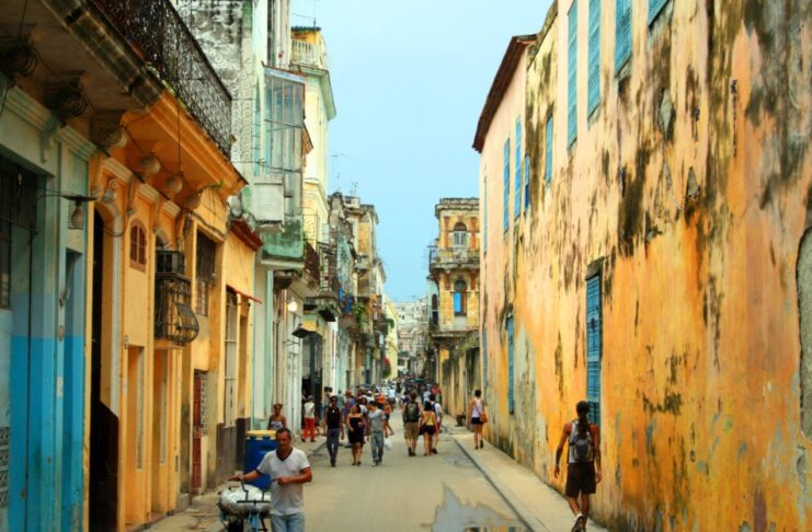 Cuba busca nuevas rutas para enfrentar su crisis económica Vista de una calle tradicional de La Habana, Cuba, con edificios antiguos de fachadas desgastadas y personas caminando en un entorno urbano característico de la isla.