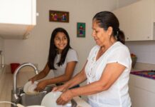 La costumbre que estamos perdiendo… y que puede cambiar una familia Una mujer y una adolescente lavan los platos juntas en la cocina de su hogar mientras conversan y sonríen, reflejando la importancia de compartir tiempo en familia.