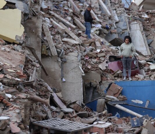 Delcy Rodríguez anuncia plan de recuperación tras los sismos y pide levantar sanciones a Venezuela Mujer de pie entre los escombros de edificios derrumbados por los terremotos en Venezuela, con estructuras colapsadas y labores de recuperación en el lugar.