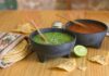¿La salsa quedó demasiado picosa? Todavía hay forma de suavizarla Dos molcajetes con salsa verde y salsa roja sobre una mesa de madera, acompañados de tortillas de maíz, totopos y un limón.
