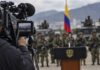 El efecto Bukele: la mano dura se convierte en espectáculo Imagen conceptual de una cámara de televisión enfocando un acto militar en Colombia, con soldados, vehículos y la bandera colombiana al fondo.