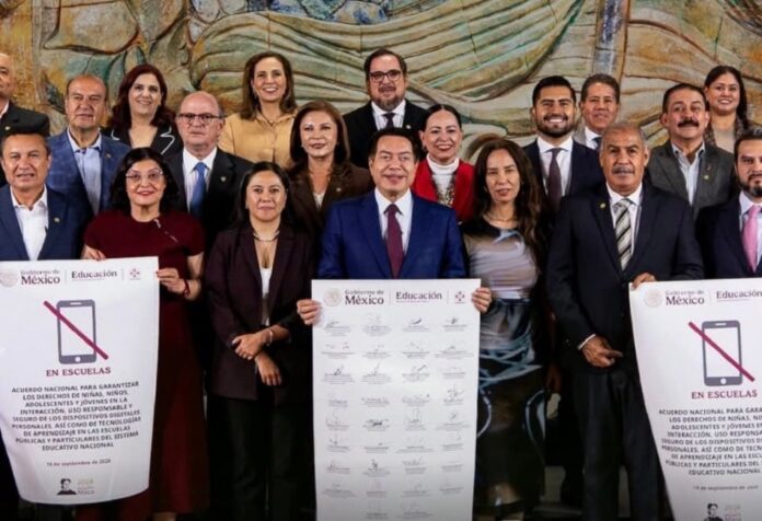 Restricción de celulares CONAEDU Mario Delgado e integrantes del Conaedu posan con el acuerdo nacional sobre el uso de teléfonos celulares en las escuelas. A los costados se observan carteles con la imagen de un celular tachado y los emblemas del Gobierno de México y la Secretaría de Educación Pública.